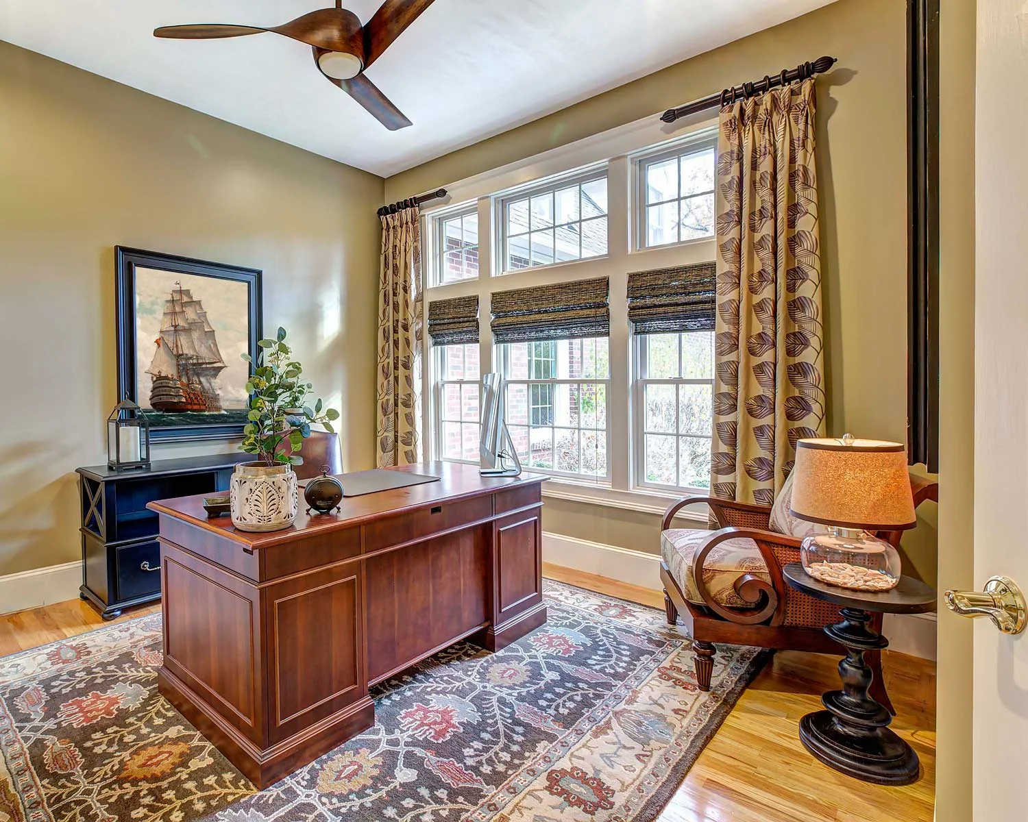 The office has a cherry desk, custom draperies and a hand knotted area rug in brown, terracotta and blue.