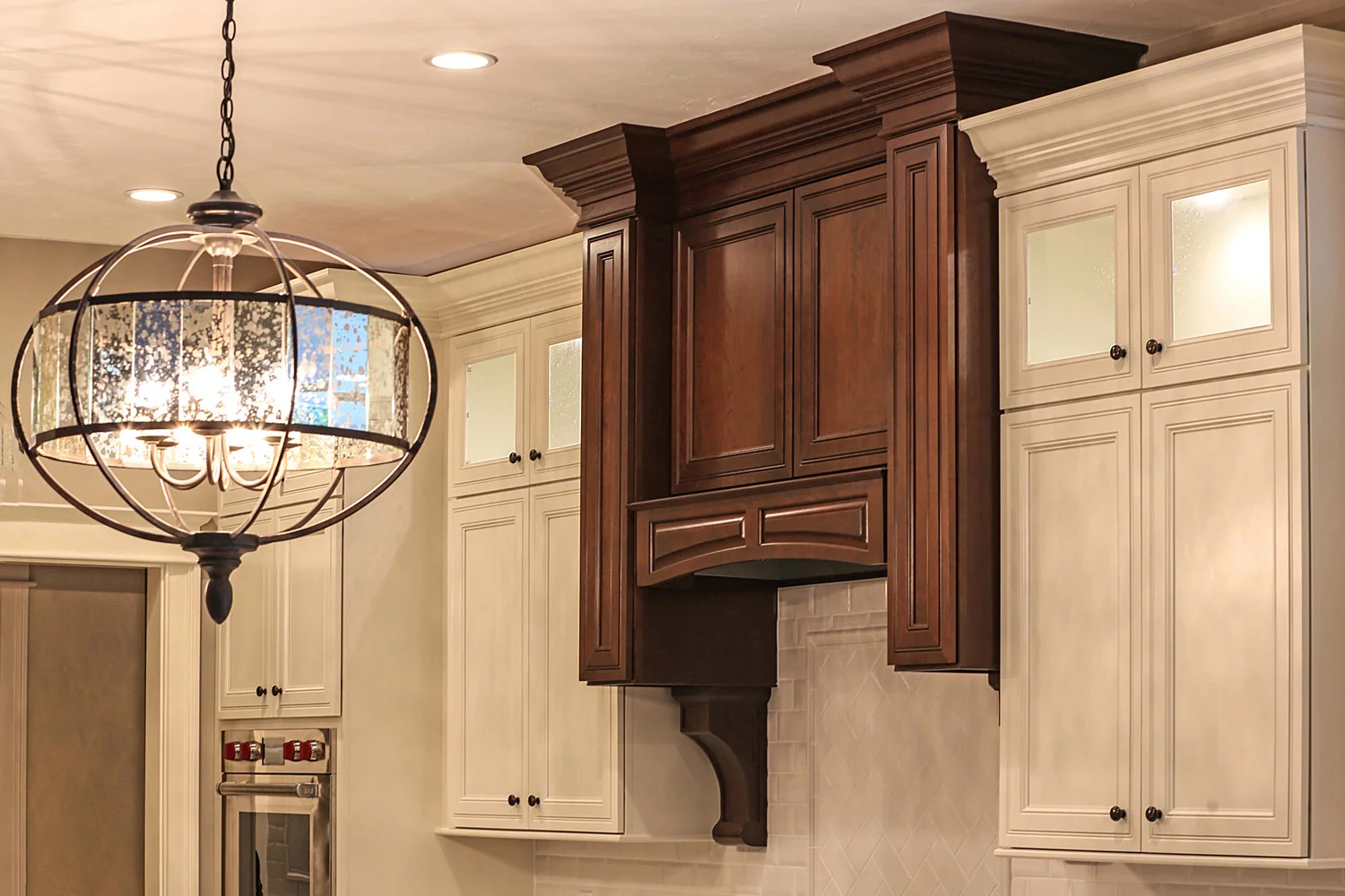 Off-white cabinets contrast range hood with corbels in Espresso finish.