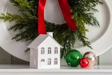 white harbor view putz house in front of a white platter and greenery wreath with red, green and silver vintage ornaments next to it.