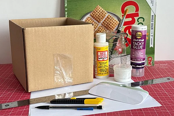 putz house base supplies: cardboard and cereal boxes, carton knife, ruler, paper, glue and paintbrush.