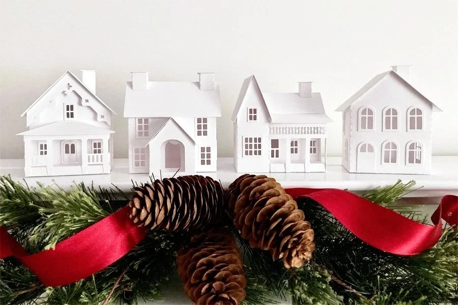 White coastal New England Village houses on a white mantel with a pinecone and greenery garland hanging below the mantel.
