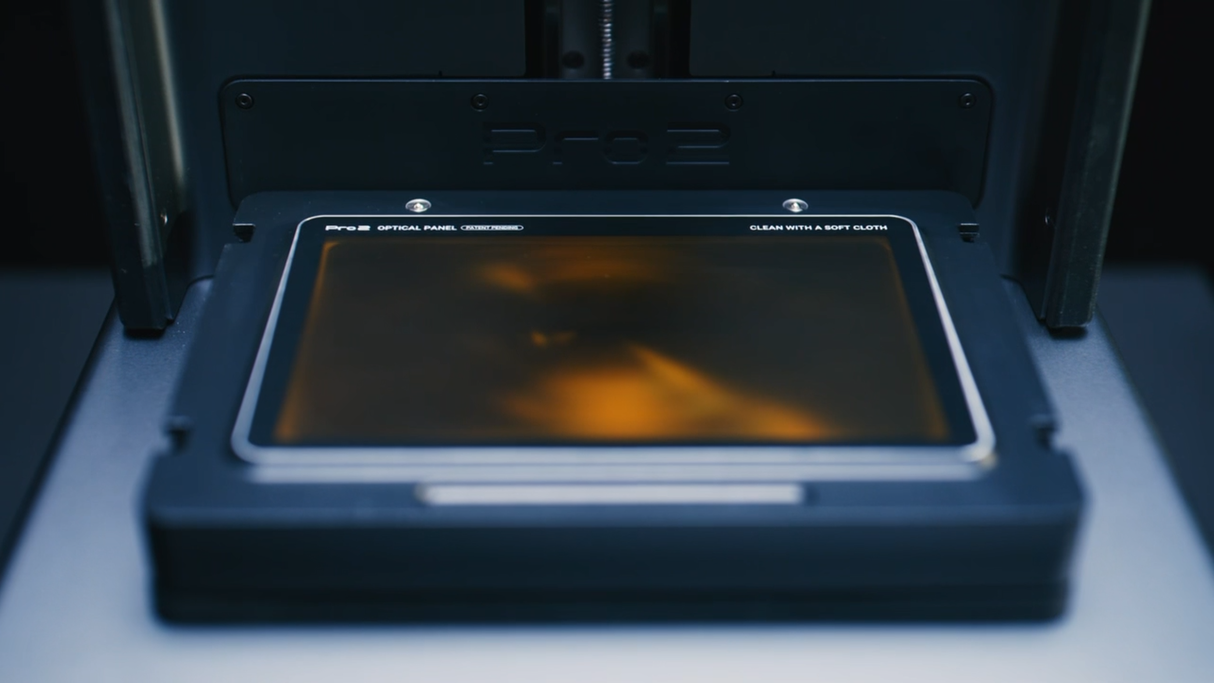 A 3D printer with a screen displaying orange and black colors, labeled 'Pro3 Optical Panel,' in a dark room.