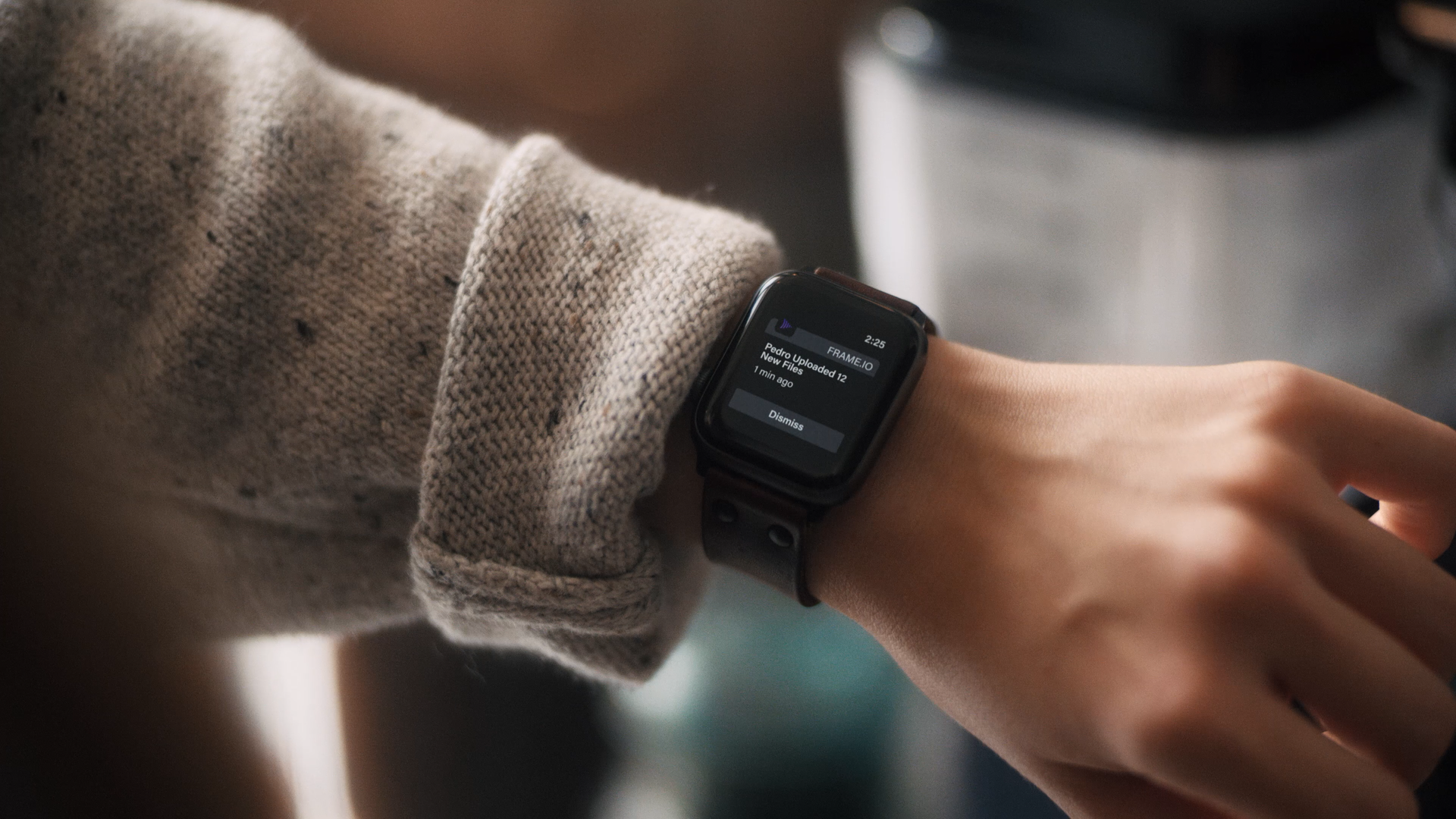 Person wearing a beige knitted sweater and a smartwatch showing a notification about uploaded files, pointing at the watch on their wrist.