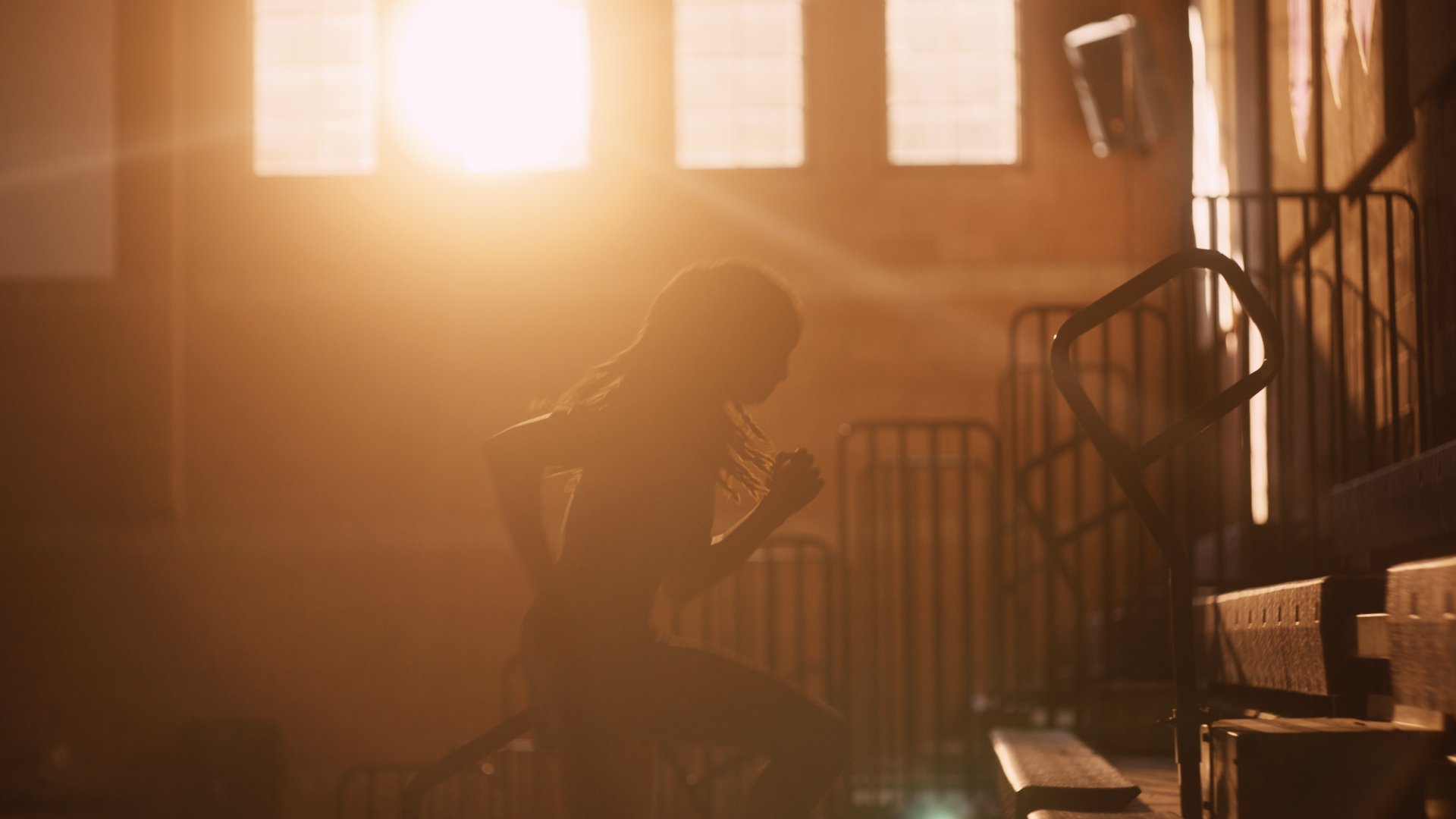 A person sitting on stairs with clasped hands and bowed head, illuminated by warm sunlight streaming through windows.