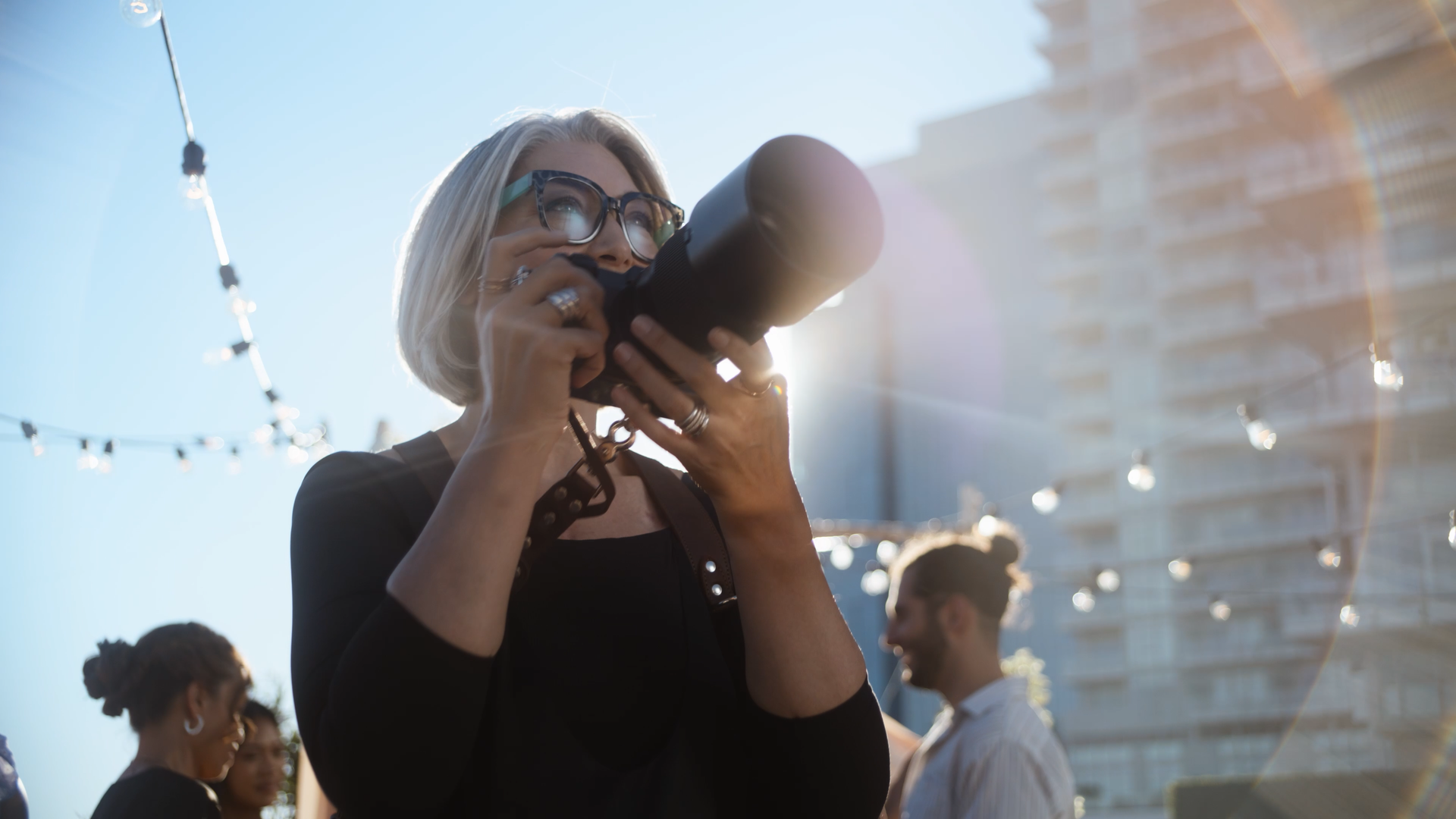 Woman with glasses taking a photo with a camera outdoors.