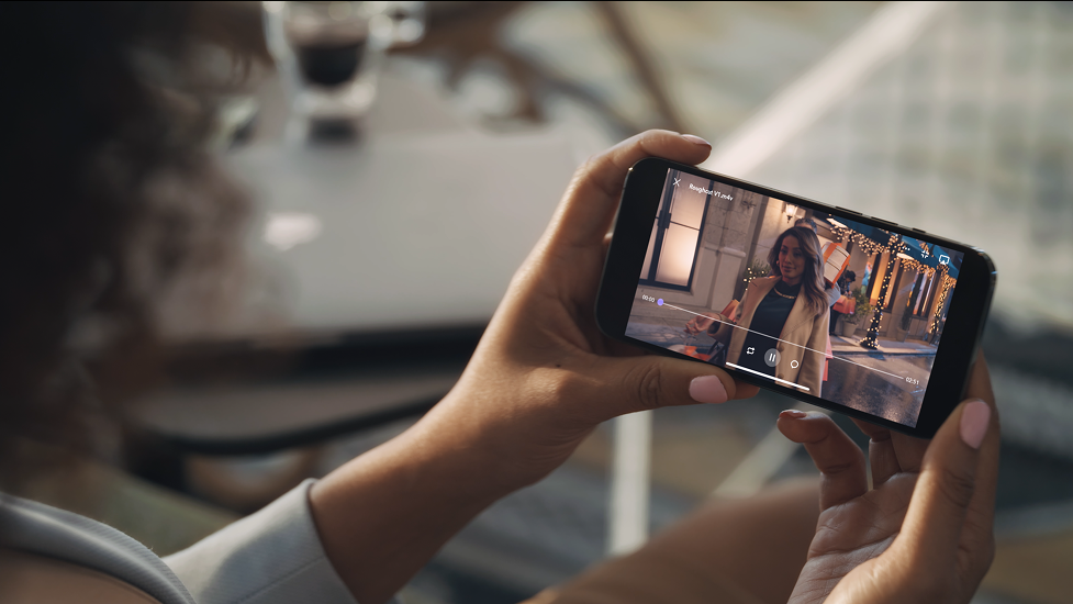 Person watching a video on a smartphone indoors with decorative lights in the background.