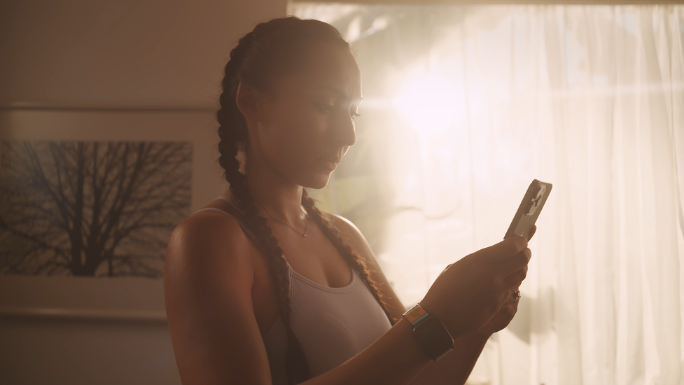 A woman with braided hair looking at her phone in a brightly lit room