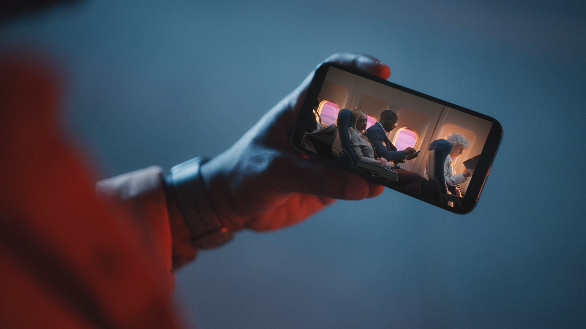Person holding a smartphone showing three passengers on an airplane, with sunset visible through the windows.
