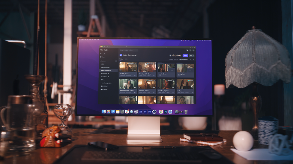 Computer monitor displaying editing software, on a wooden desk with decorative objects and a vintage lamp.