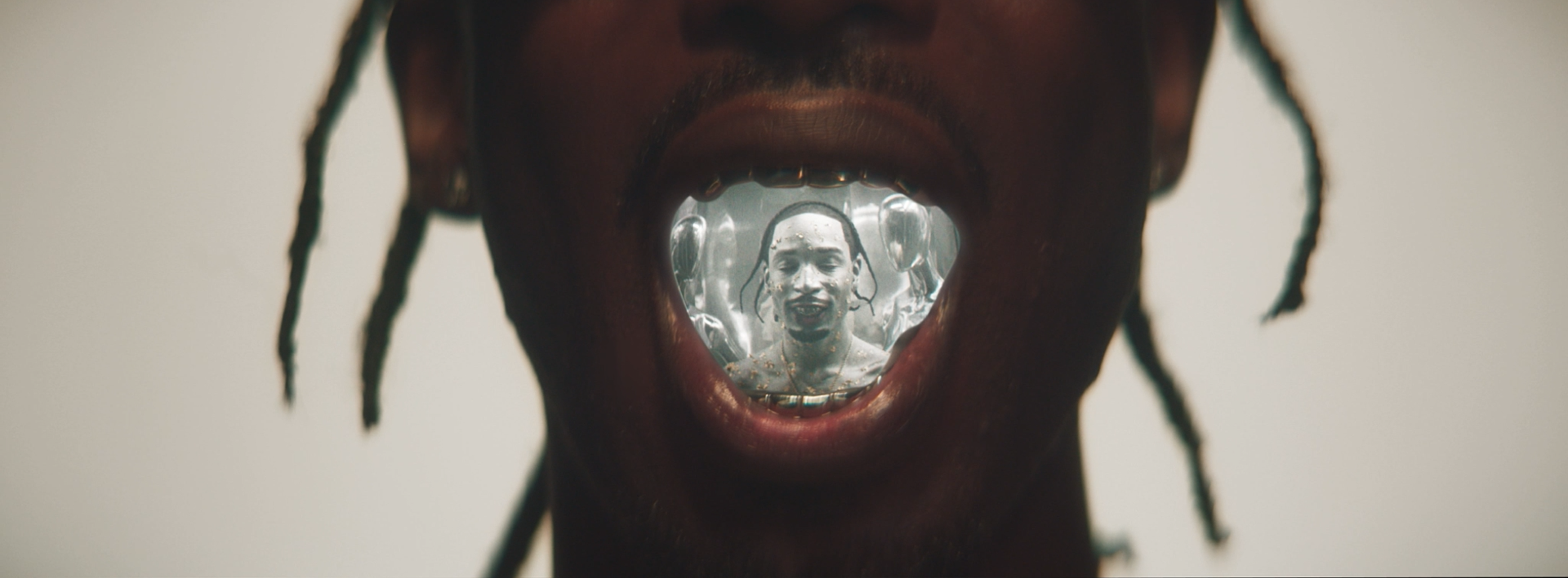 Close-up of a person's open mouth with a reflective surface inside, showing their face and a background of balloons.