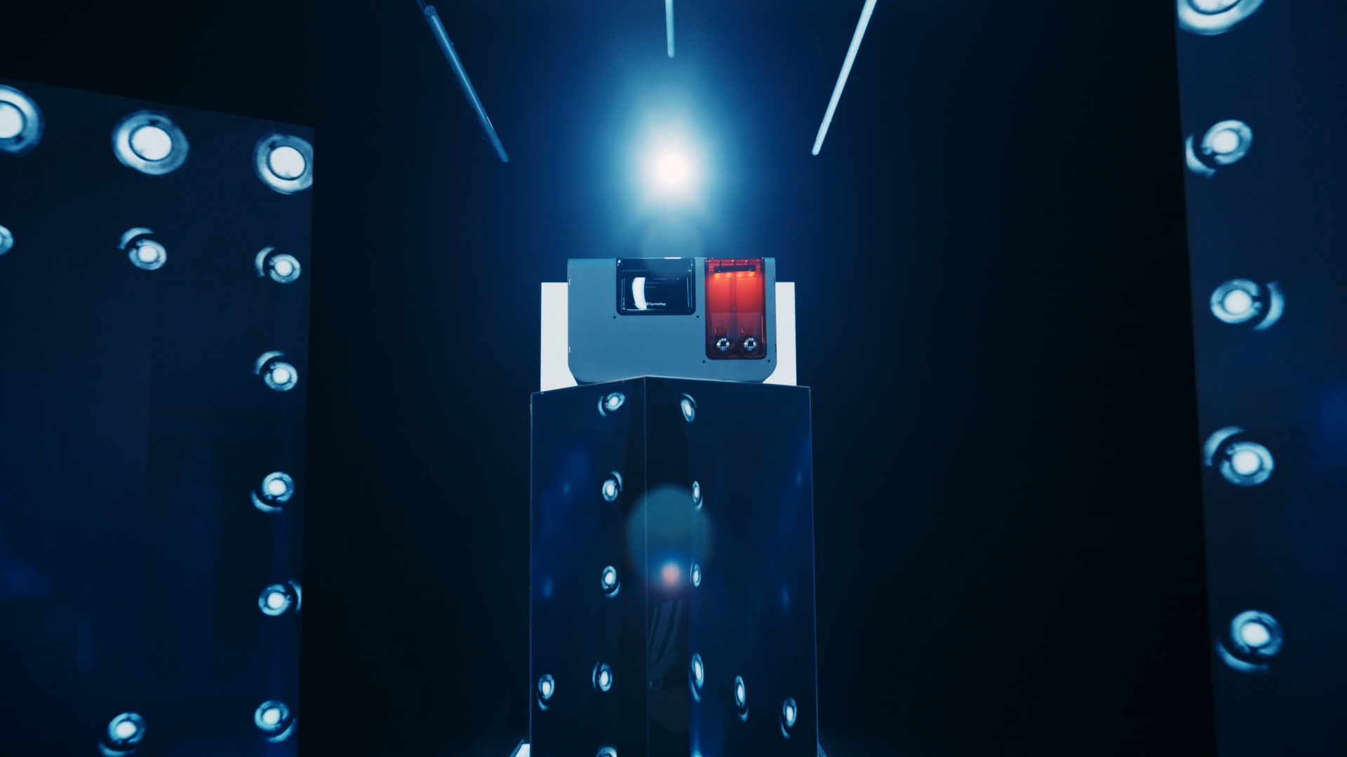 A vintage typewriter with a red ribbon is displayed on a pedestal under blue and white lighting in a dark room fitted with reflective panels.
