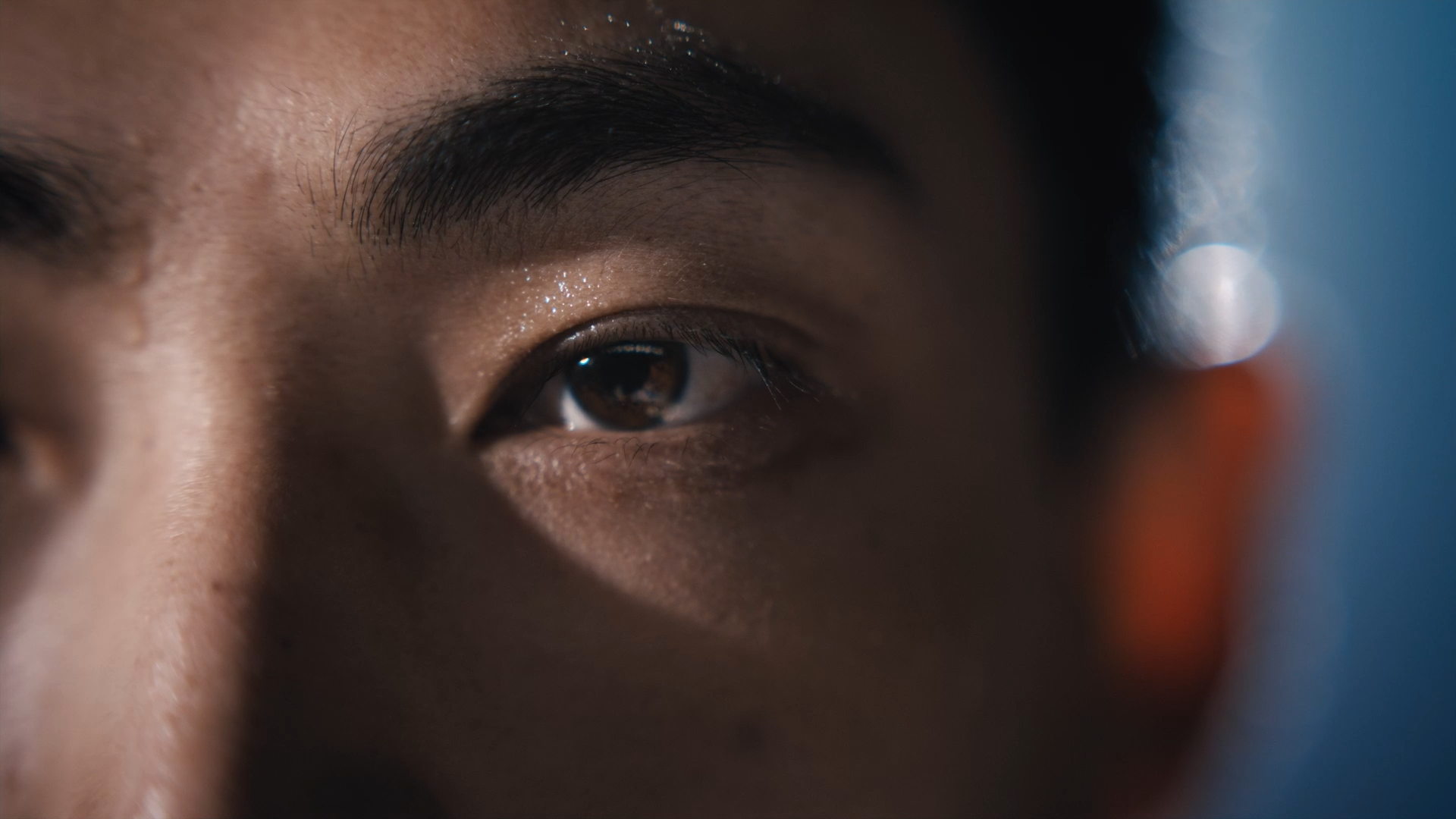 Close-up of a person's eye and eyebrow, with detailed skin texture and a bokeh background.