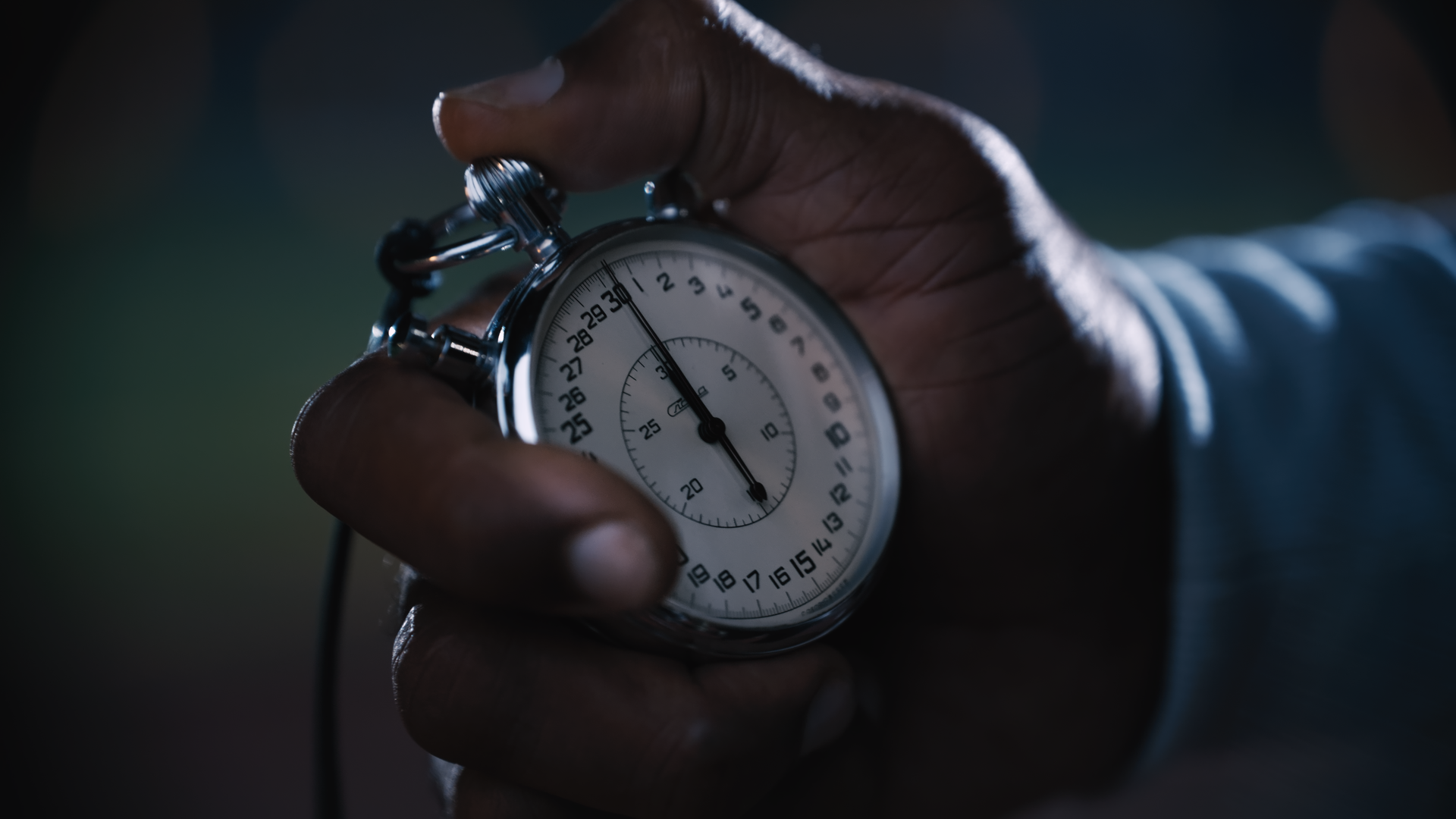 Close-up of a hand holding a stopwatch with a dark blurred background.