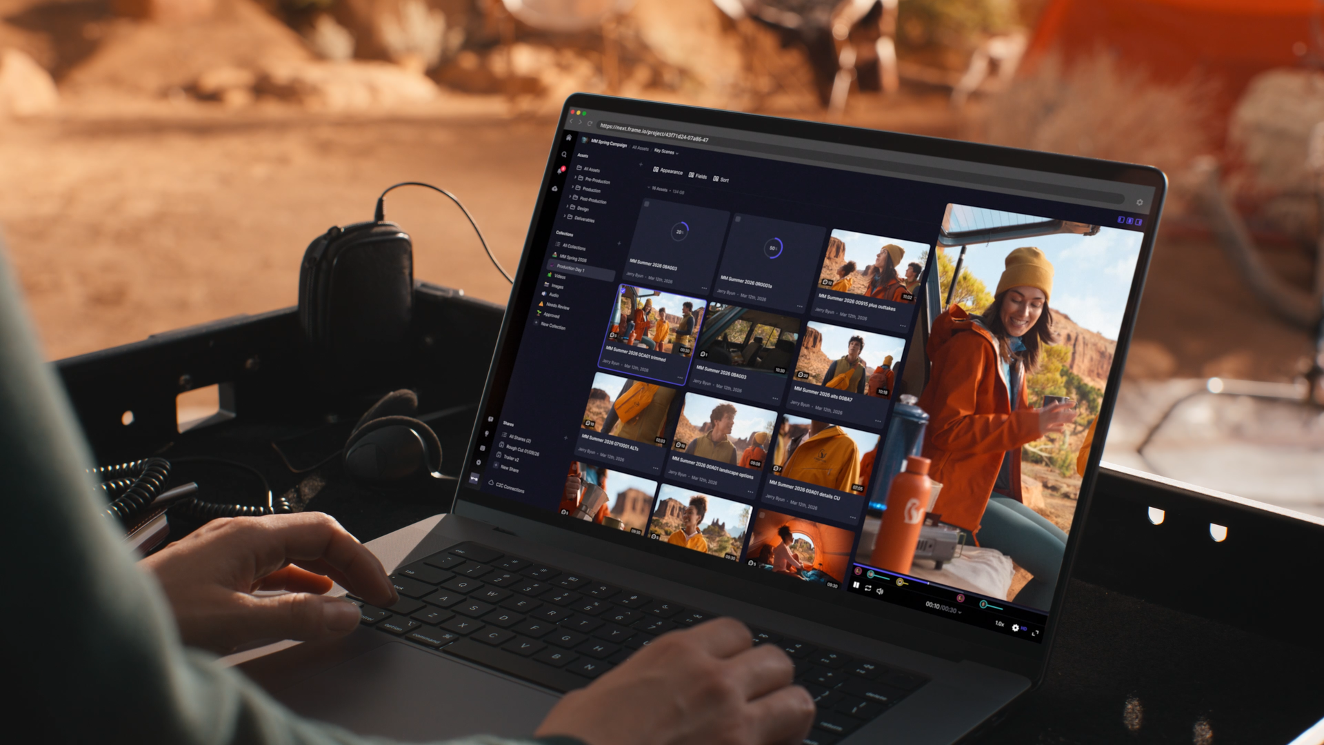 A person working on a laptop outdoors with a desert landscape in the background, editing video footage of a woman in an orange jacket and yellow beanie.