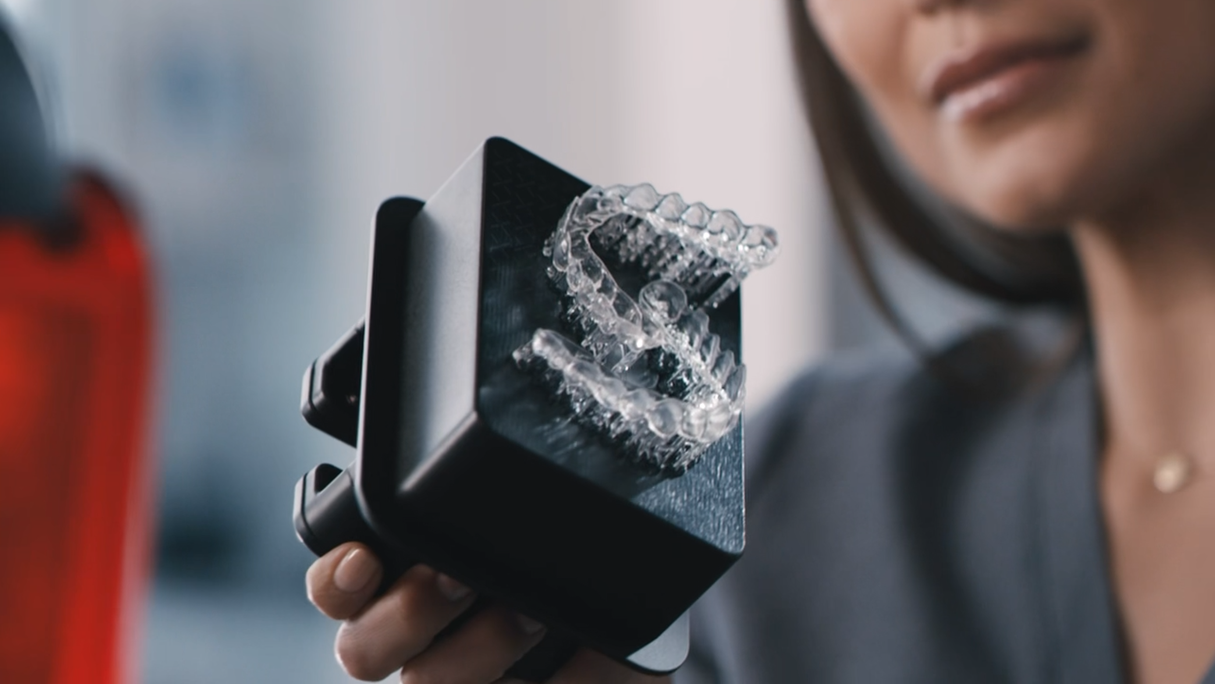 Close-up of a person holding a smartphone with a dramatic effect where the screen shows a 3D model or digital rendering of a human jaw and teeth, possibly made of glass or transparent material.