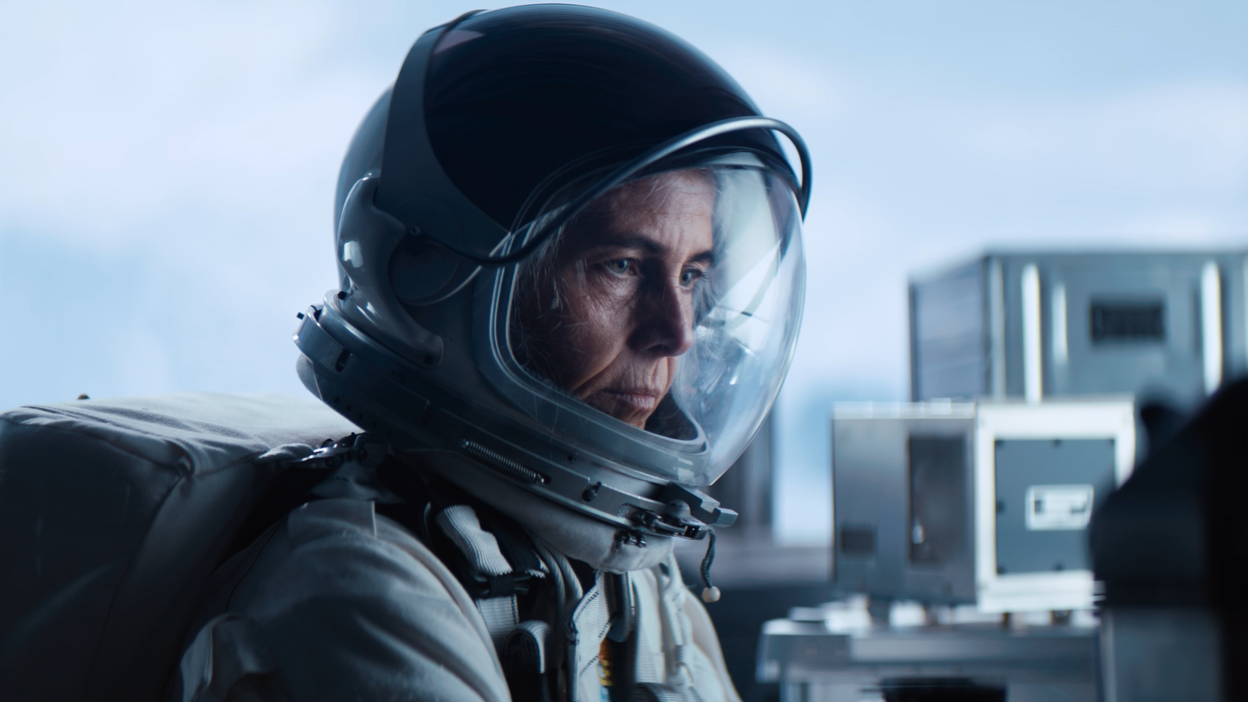 Close-up of a female astronaut wearing a helmet and space suit, with a focused expression, in a spacecraft or space station interior.