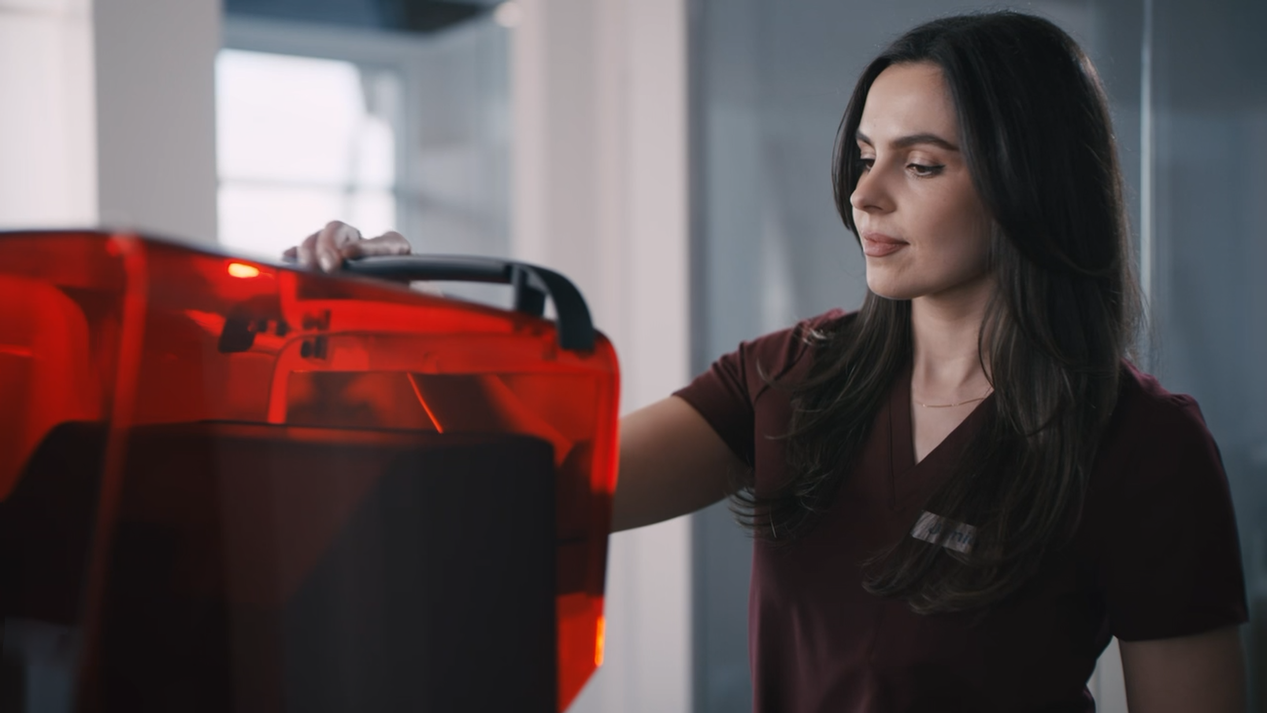 A woman with dark hair in a medical uniform collecting a sample from a red medical device.