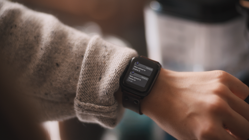 Close-up of a person's left wrist wearing a smartwatch displaying notifications about file uploads, with the person wearing a beige or light brown knitted sweater.