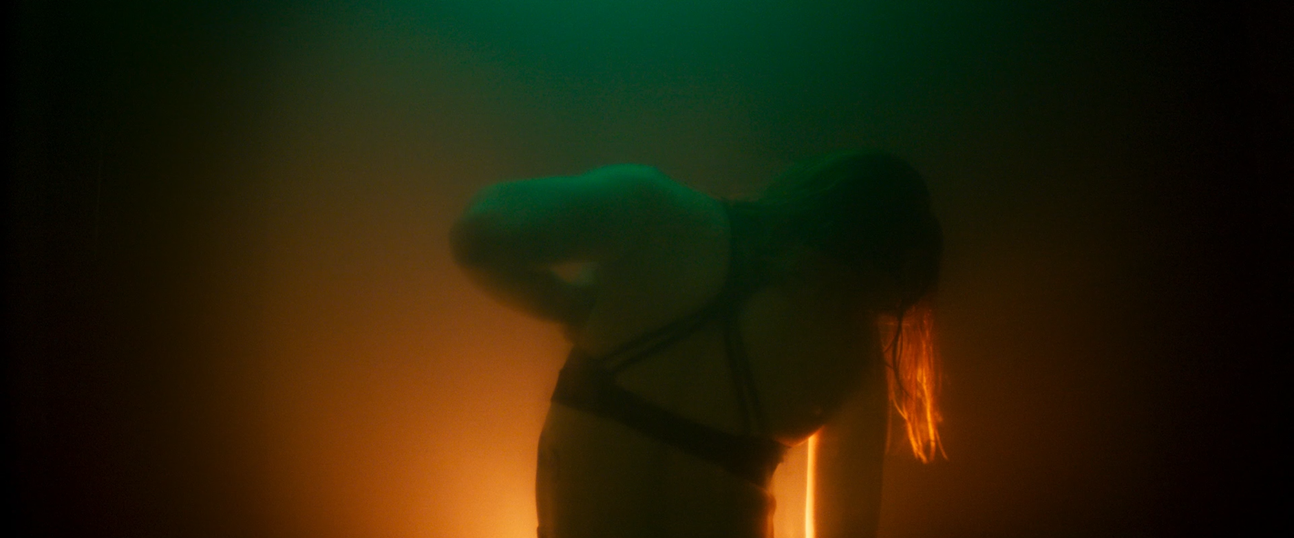 Silhouette of a person with long hair illuminated by colorful, low-light background, appearing to be in a dance or expressive pose.