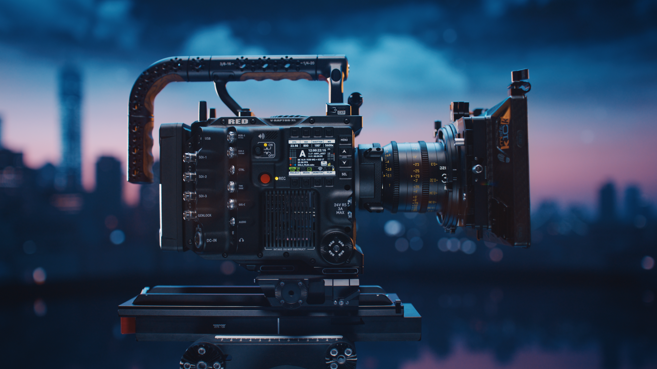 A professional cinema camera with a large lens mounted on a tripod against a sunset skyline with dark clouds.