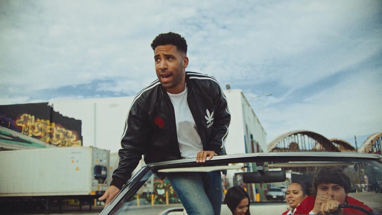 Man standing on the roof of a car at a carnival, with others inside and behind the vehicle.