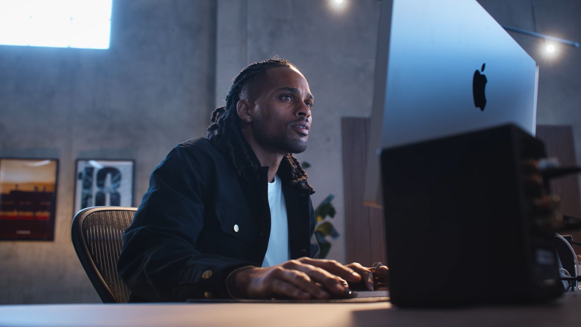 A man with dreadlocks working on a computer in a modern office.