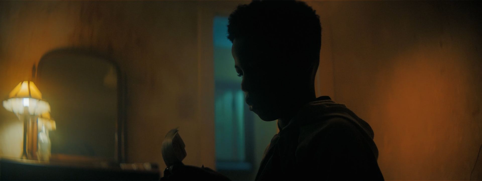 Silhouette of a person reading a book in a dimly lit room with a table lamp
