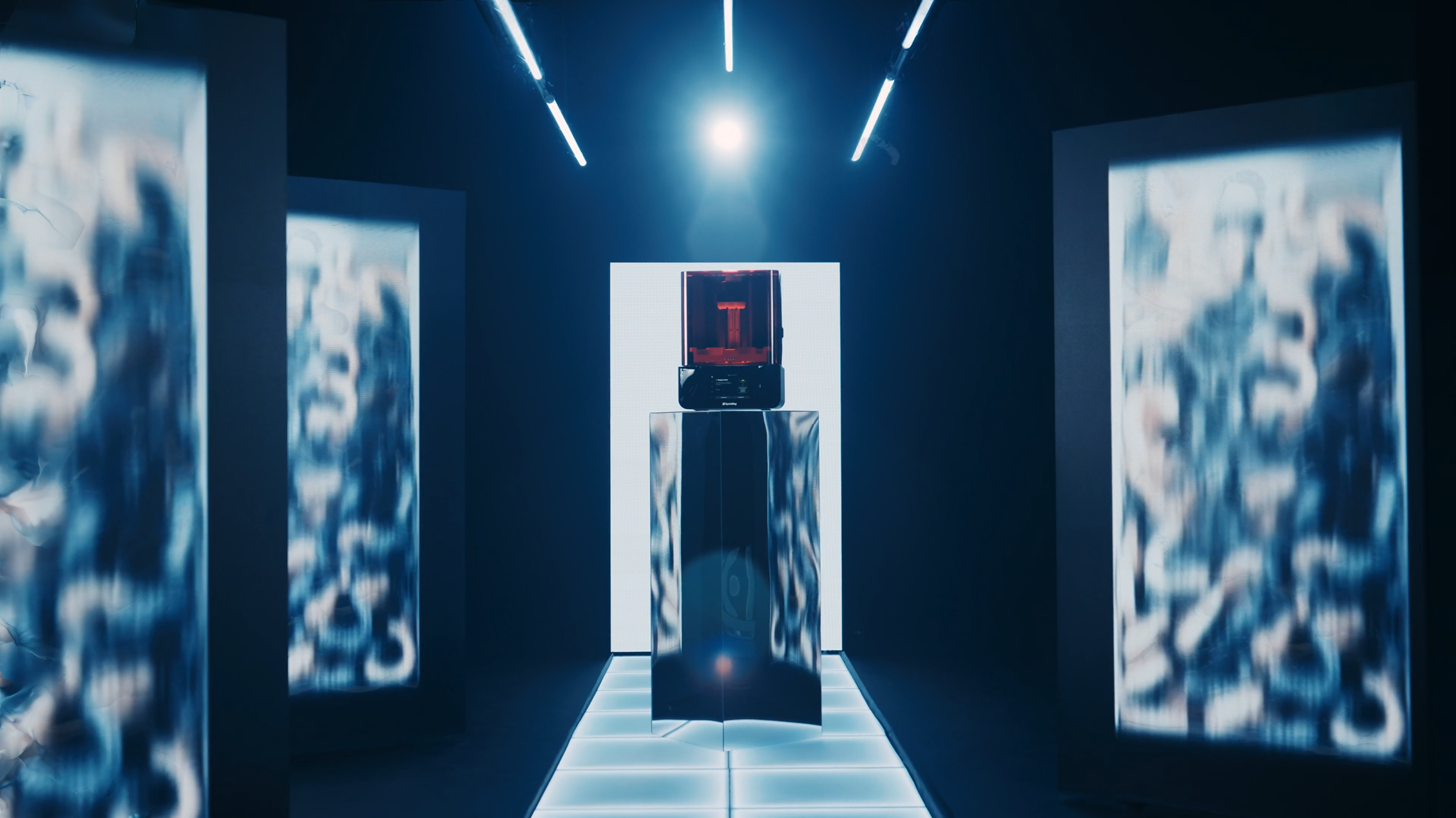 A futuristic exhibit space with metallic and digital display elements, featuring a central red and black vending machine or display unit, illuminated by blue ambient lighting and fluorescent lights overhead.