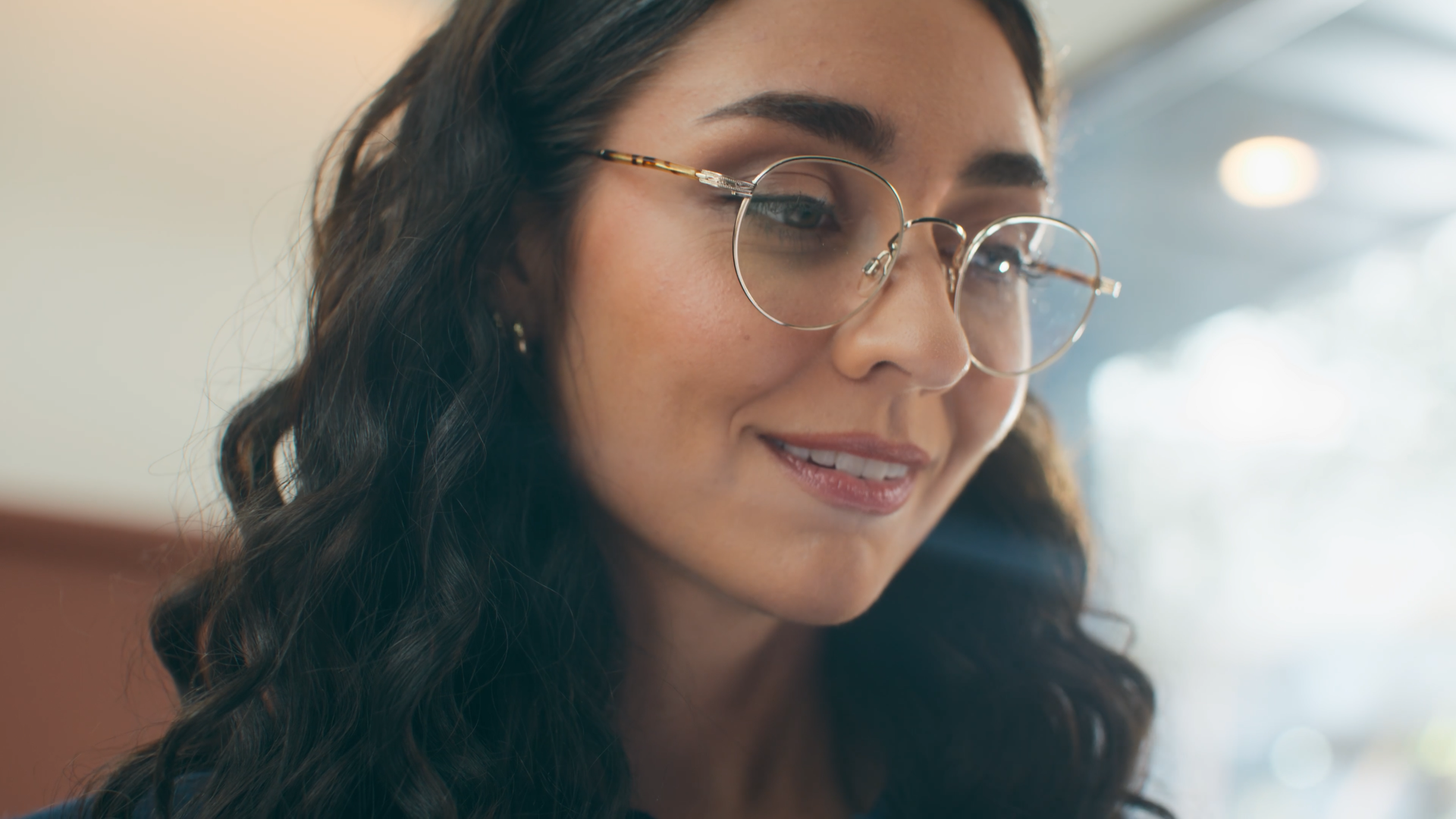 A smiling woman wearing round eyeglasses with curly dark hair.