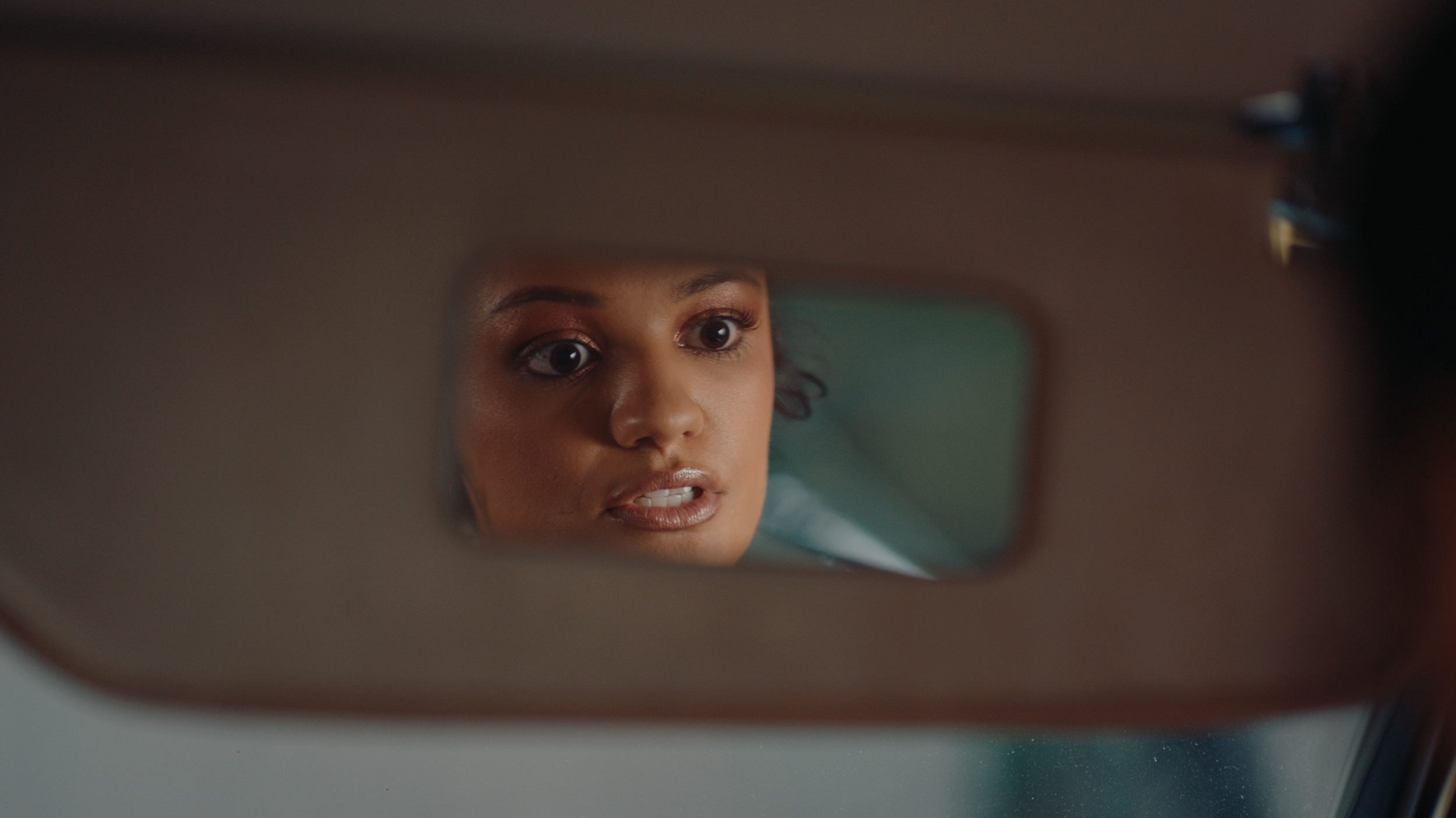 A woman with makeup looking into a car's rearview mirror.