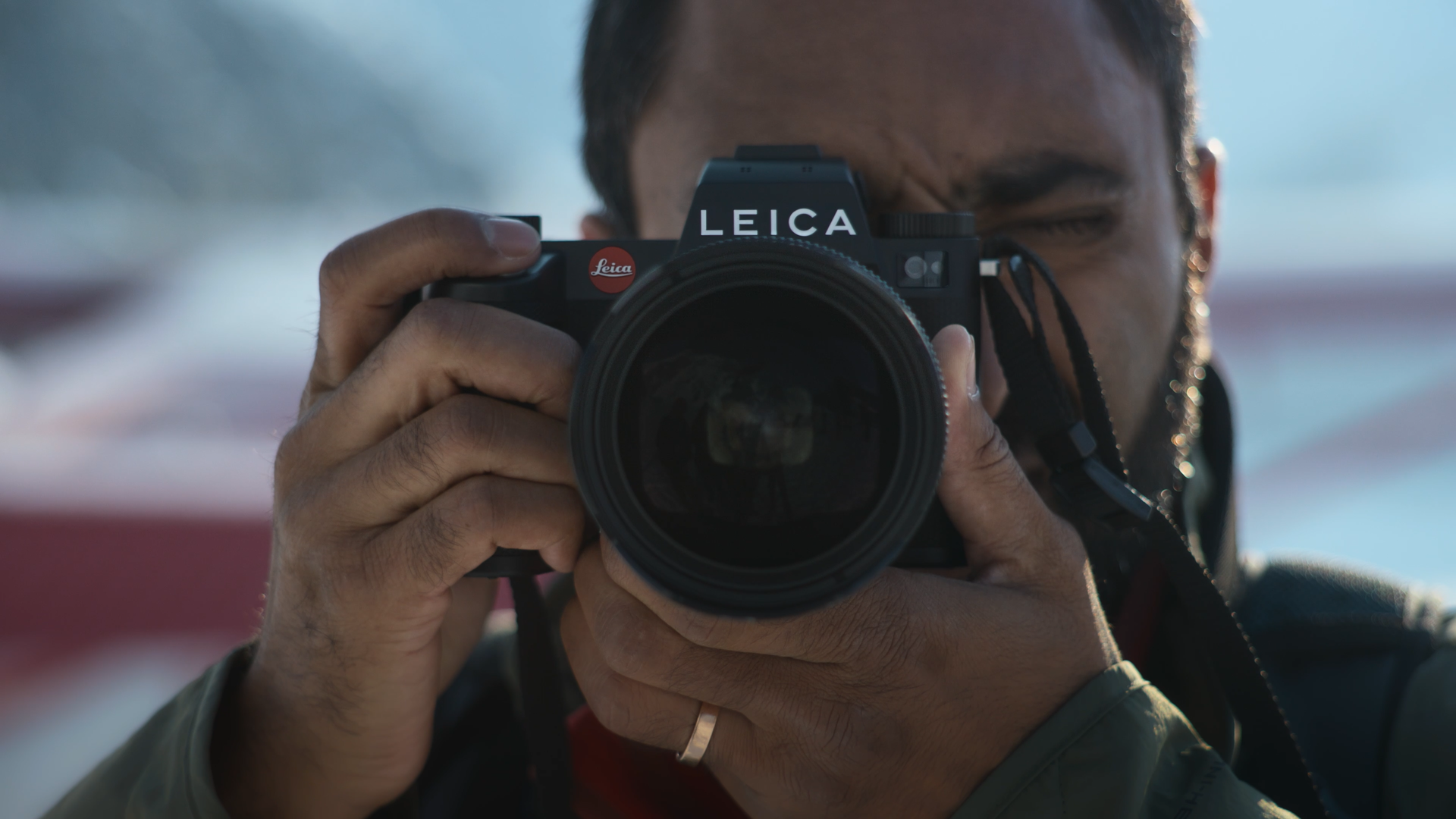 Person taking a photograph with a Leica camera, holding it up to their eye with their right hand, with a blurred background.