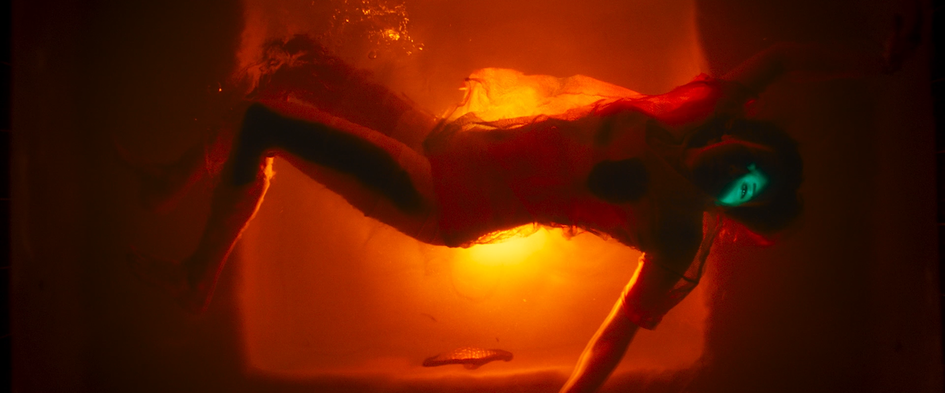 A doll with glowing blue eyes, dressed in dark clothing, lying on a glowing orange surface in a dimly lit environment.