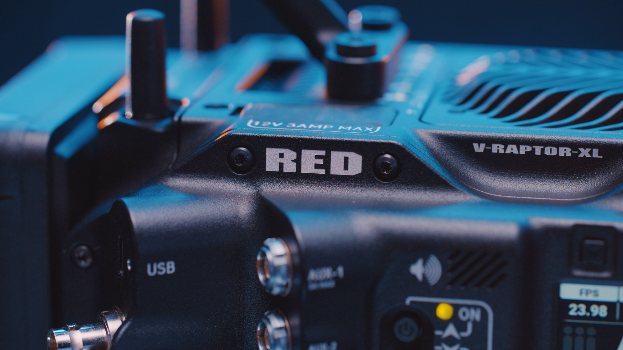 Close-up of a remote control with various buttons and labels, including 'RED', 'V-Raptor-XL,' and 'USB,' with a blurred background.