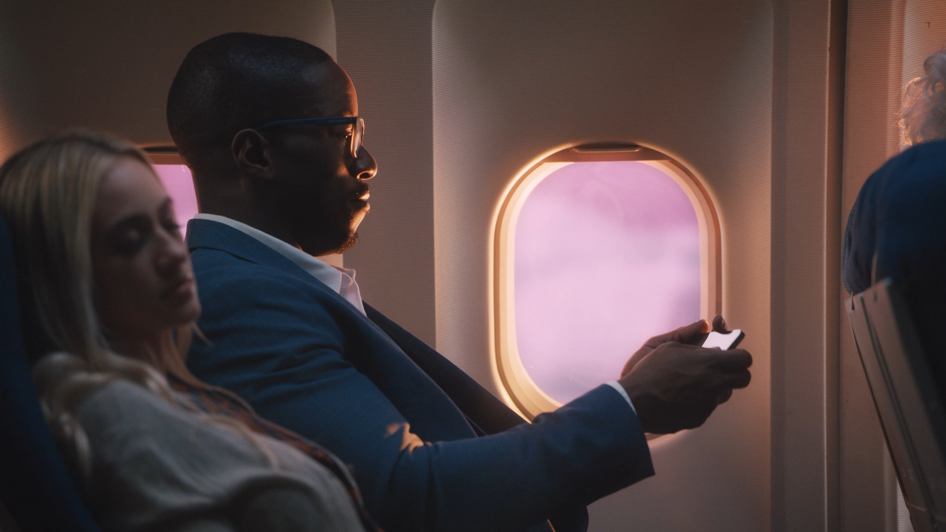 Passengers seated on an airplane, looking out the window and using their phones.