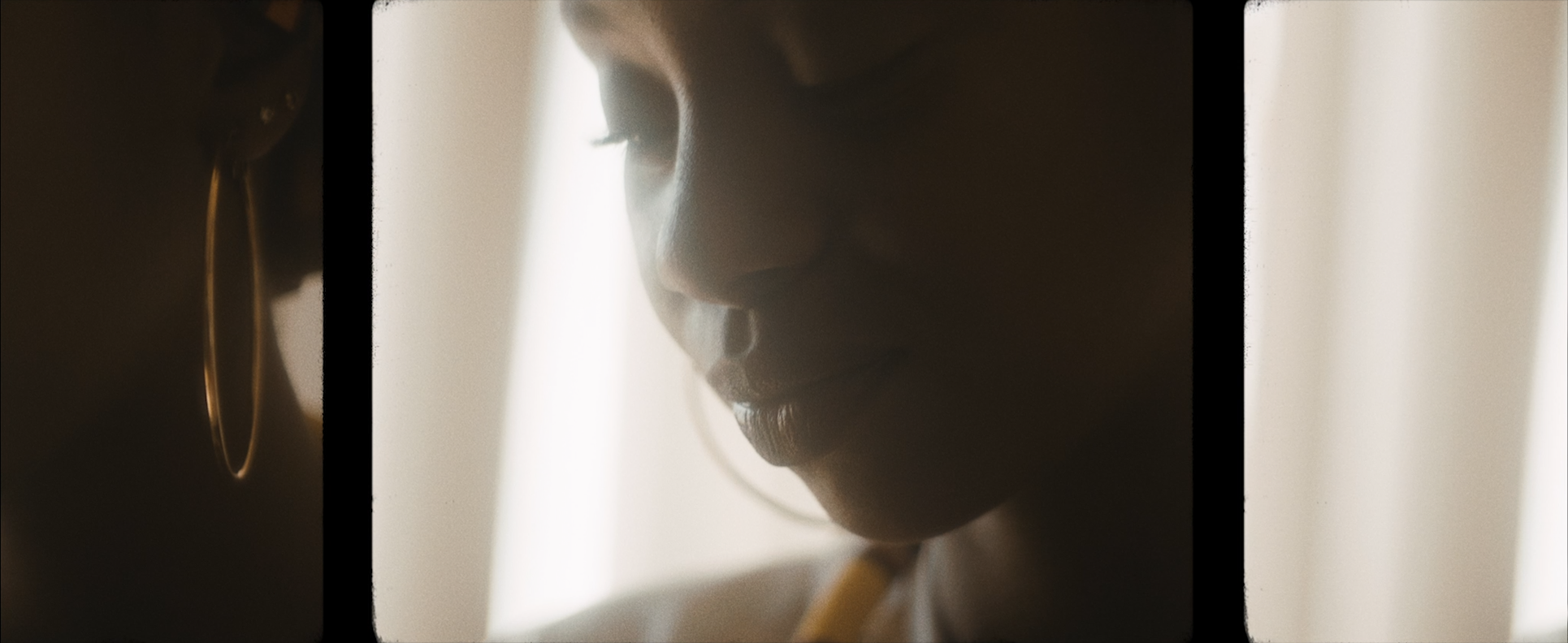 Close-up of a woman's face in profile with soft lighting, showing her nose, lips, and a gold hoop earring, with a blurred background.