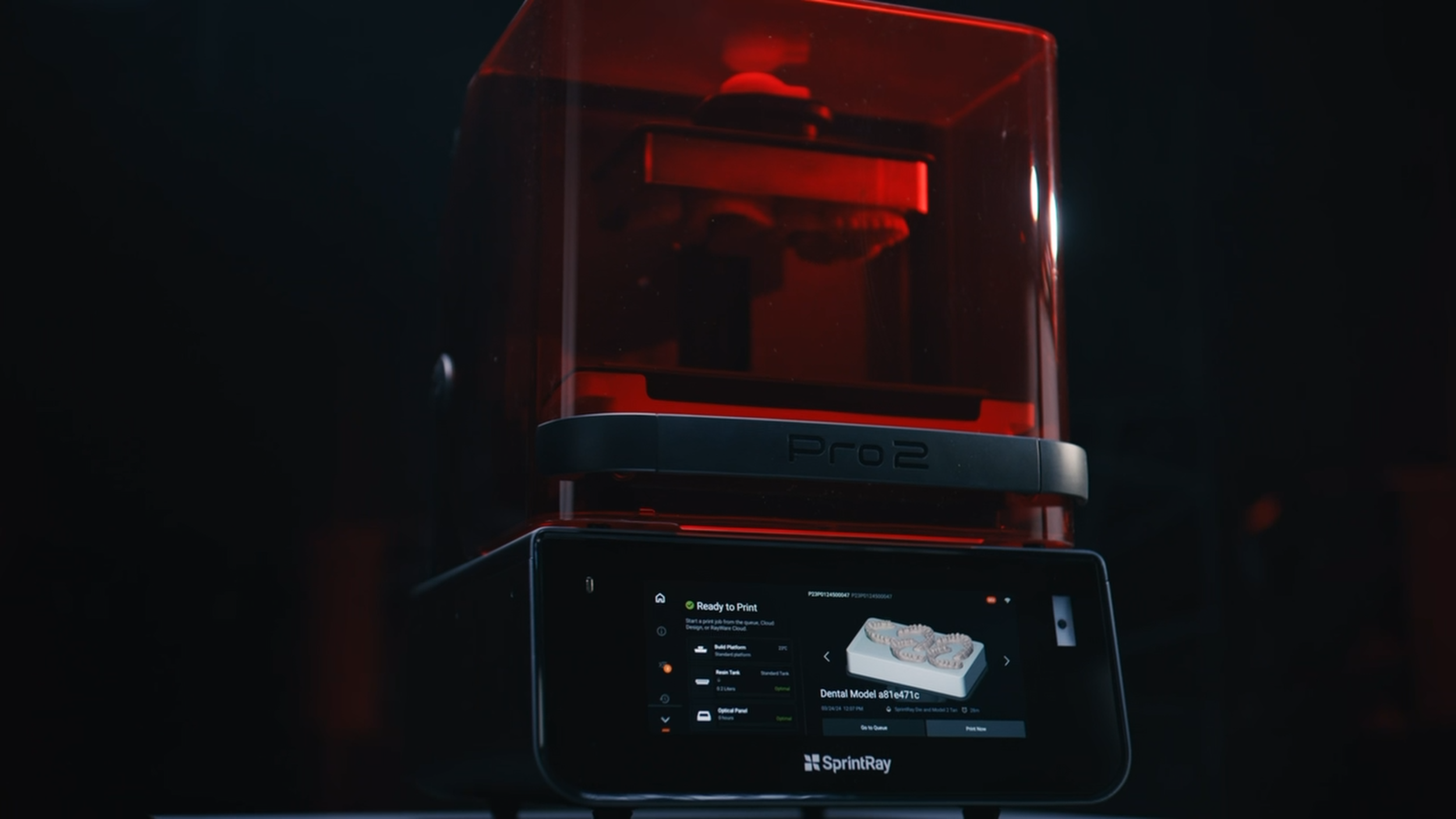 A 3D printer surrounded by a red protective case, with a digital screen displaying print progress and settings, branded 'SprintRay'.