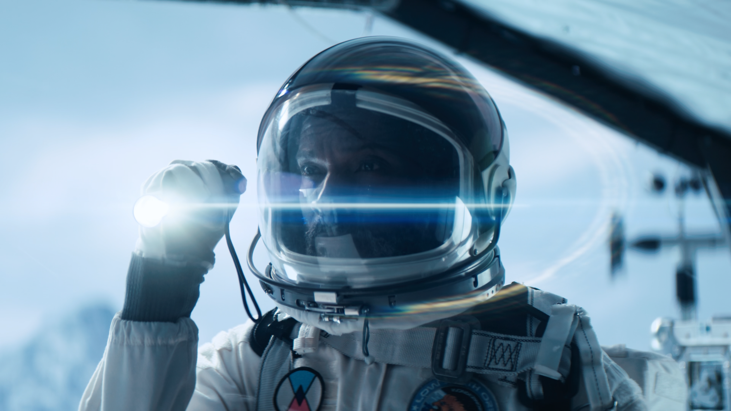Astronaut in a spacesuit adjusting their helmet, with a bright light and blue sky in the background.