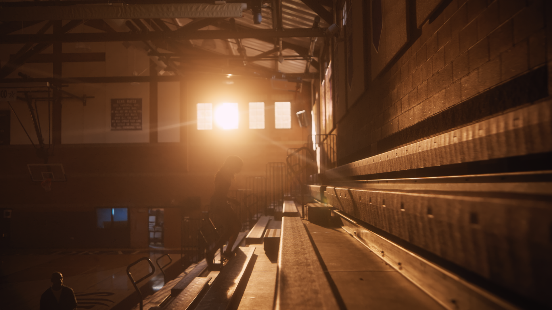 Inside a gymnasium with sunlight streaming through large windows, a person is sitting on bleachers with others around, basketball hoops and gym equipment visible.