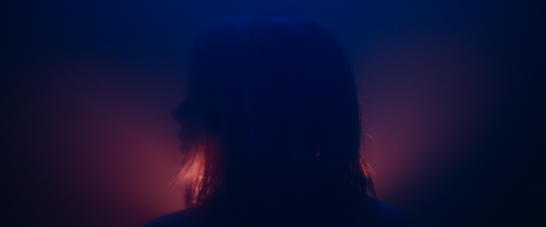Silhouette of a woman with wet hair against a dark background with pink and purple lighting.
