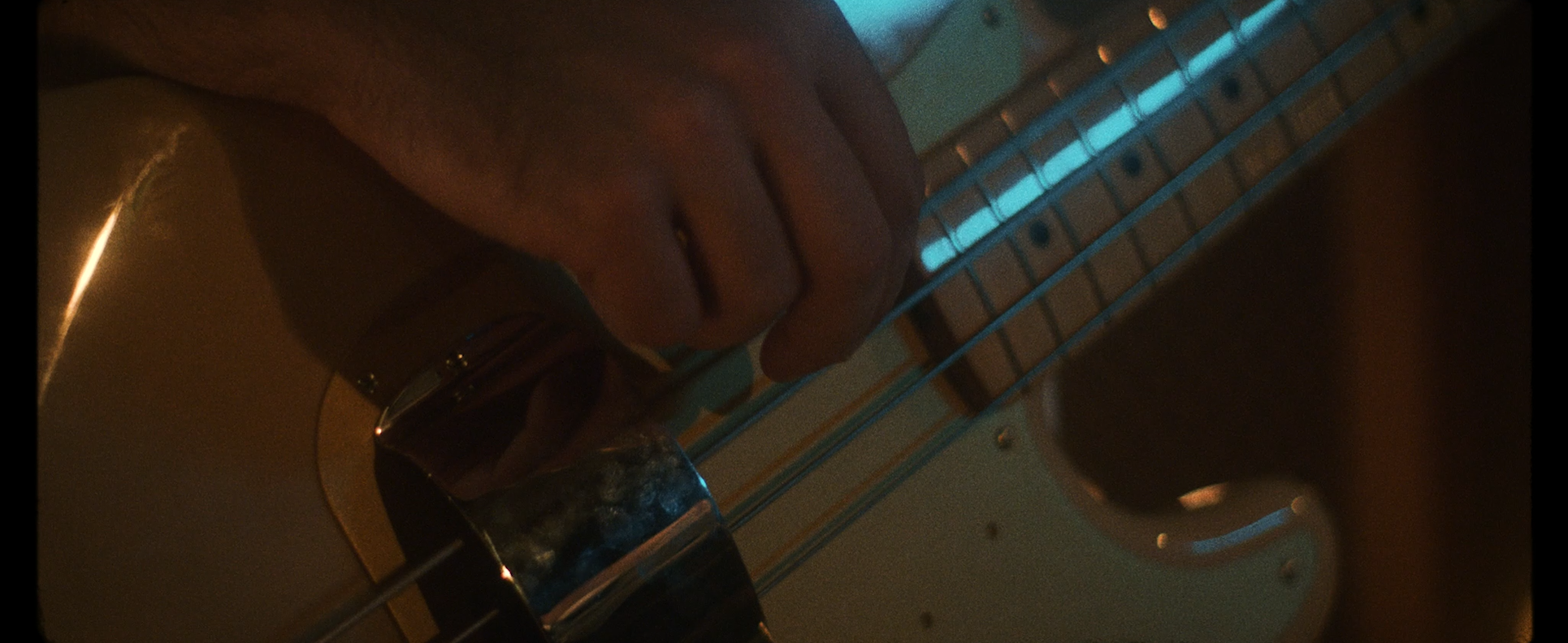 Close-up of a person's hand playing an electric guitar, with a magnetic pickup visible, in a dimly lit room.