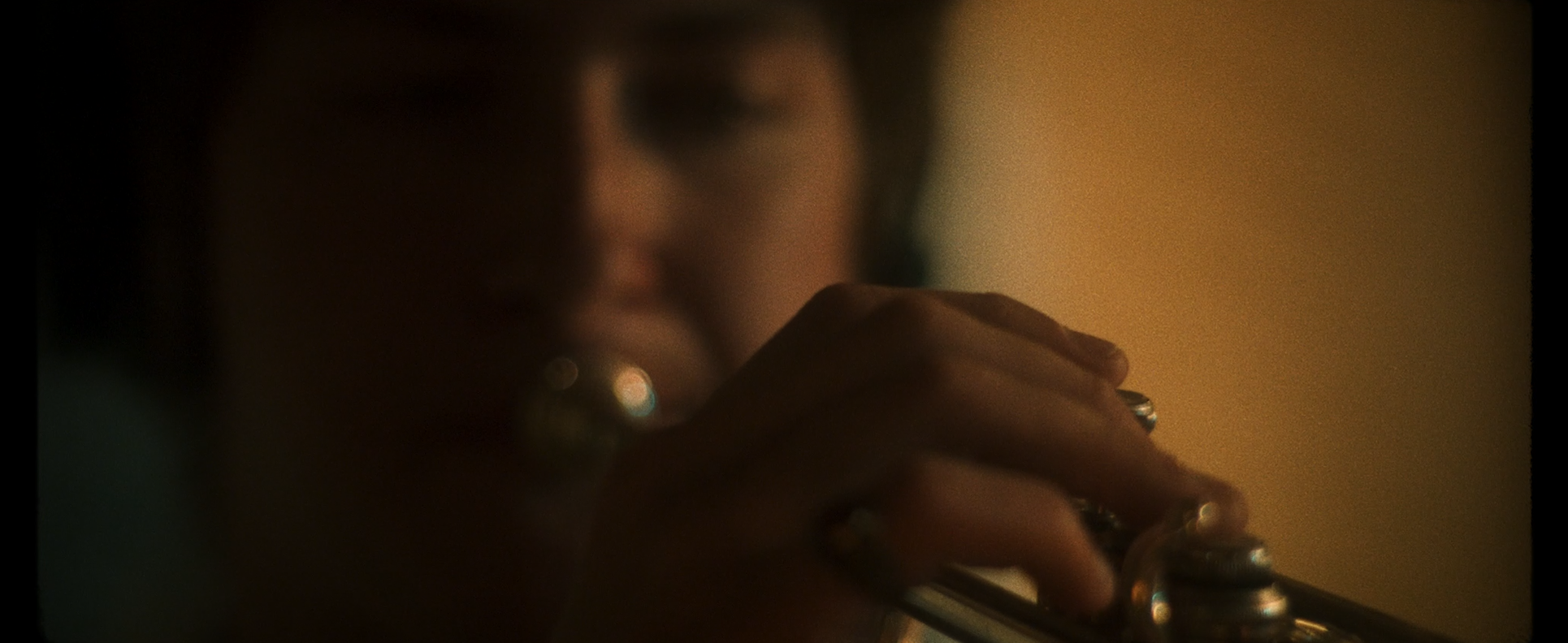 Close-up of person with dark hair playing a trumpet in dim lighting.
