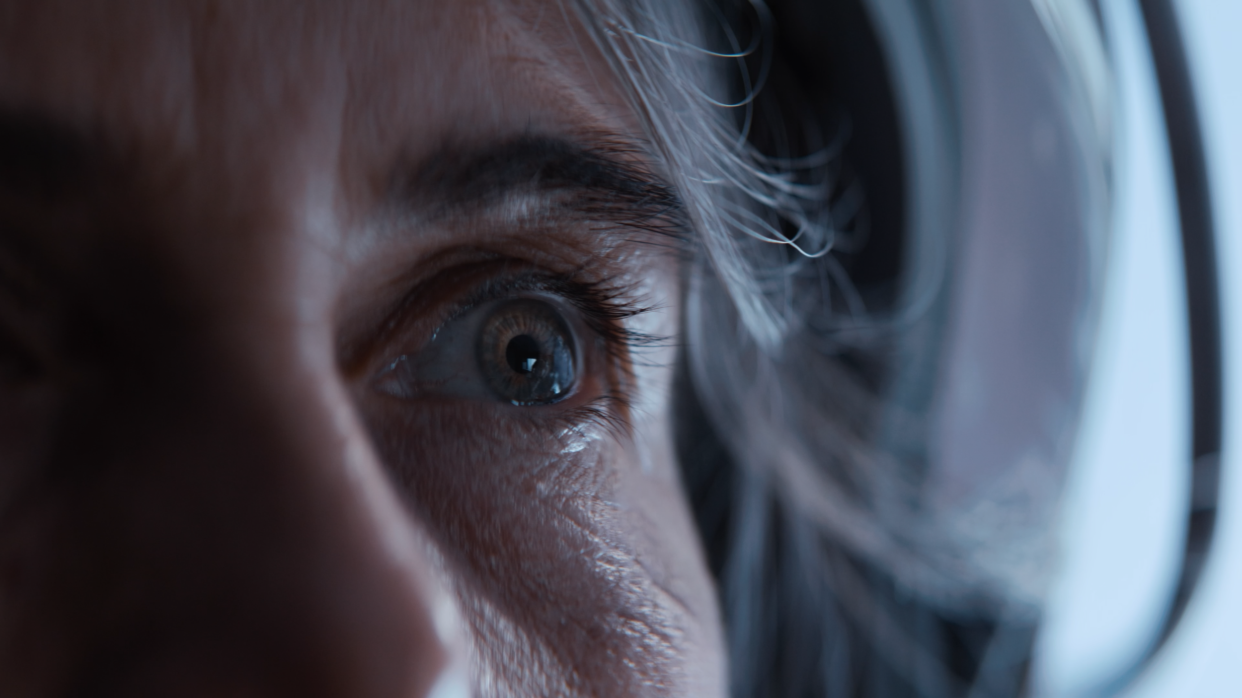 Close-up of a person's eye and eyebrows, with part of a hearing aid visible near the ear.