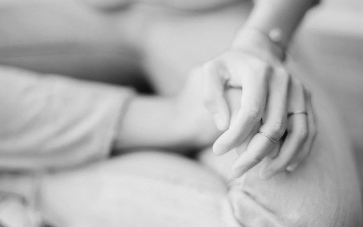 Close-up of two people holding hands, with rings on their fingers, in a heartfelt gesture.
