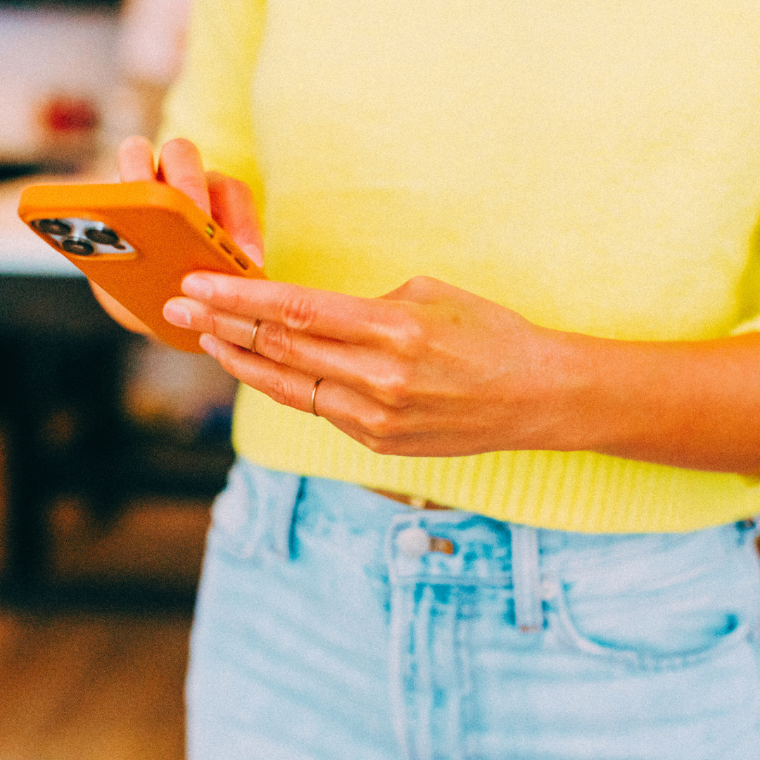 Person wearing a yellow top and light blue jeans holding an orange smartphone.