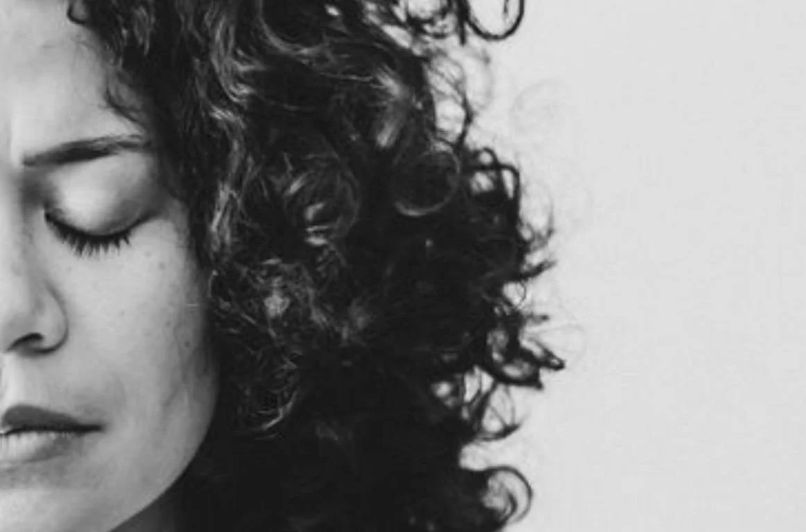 Black and white close-up of a woman with curly hair and closed eyes.