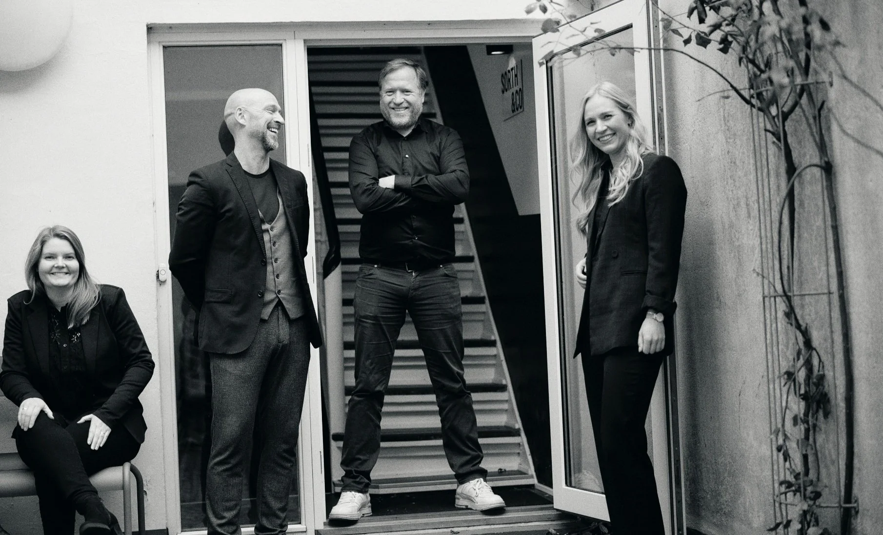 Fire kollegaer er placeret foran indgangspartiet til virksomheden SORTH & CO