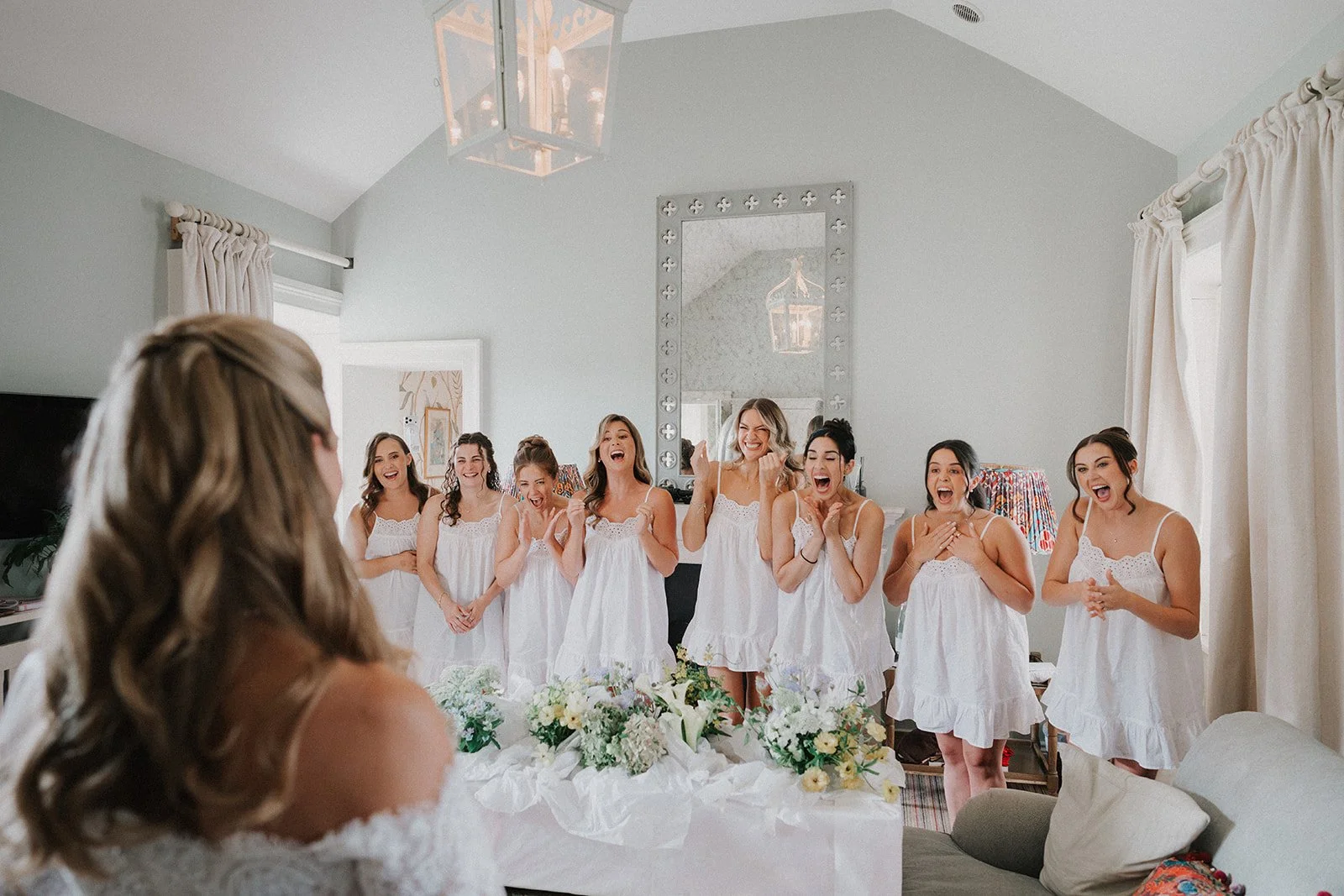 Bridesmaids smiling and cheering as they see the bride in her wedding dress.