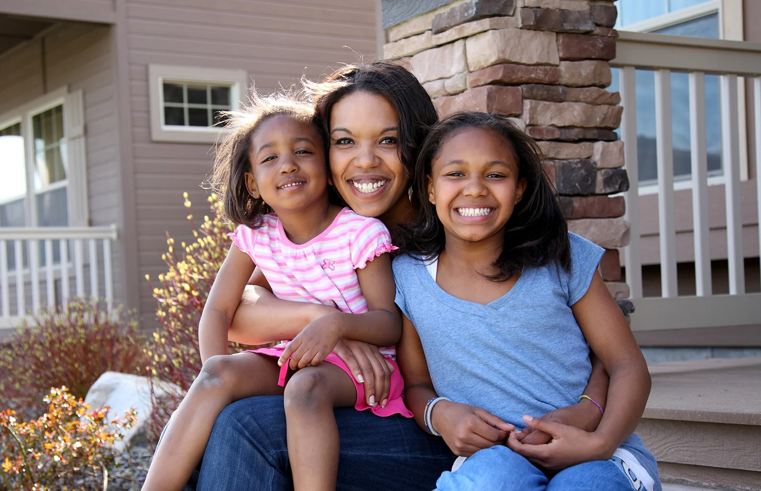 Foster family sits outside on stairs. Woman and two children.