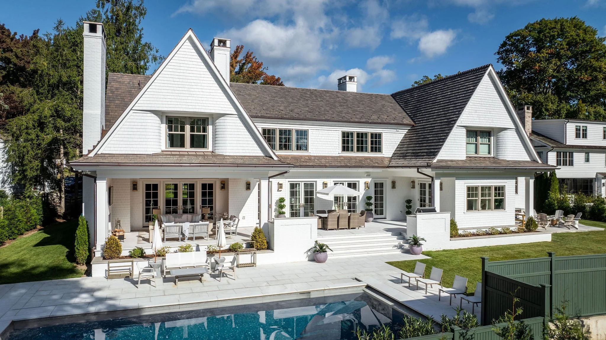 A photo of a bright white house with dark natural wood shingles on the roof shot from the backyard