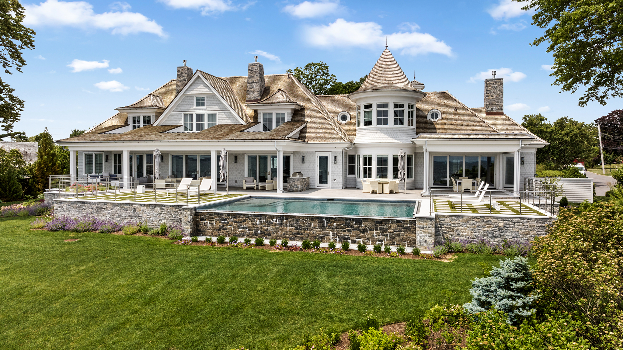 A large light grey house with an infinity pool and natural wood shingles